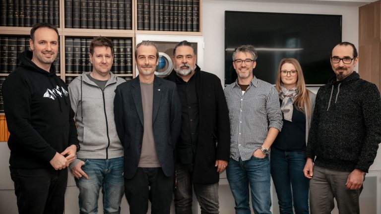 Sieben der neun Gründungsmitglieder des Fördervereins KITE e. V. bei der Gründungsversammlung – sie stehen nebeneinander in einem Raum mit Bücherregal und Bildschirm im Hintergrund.